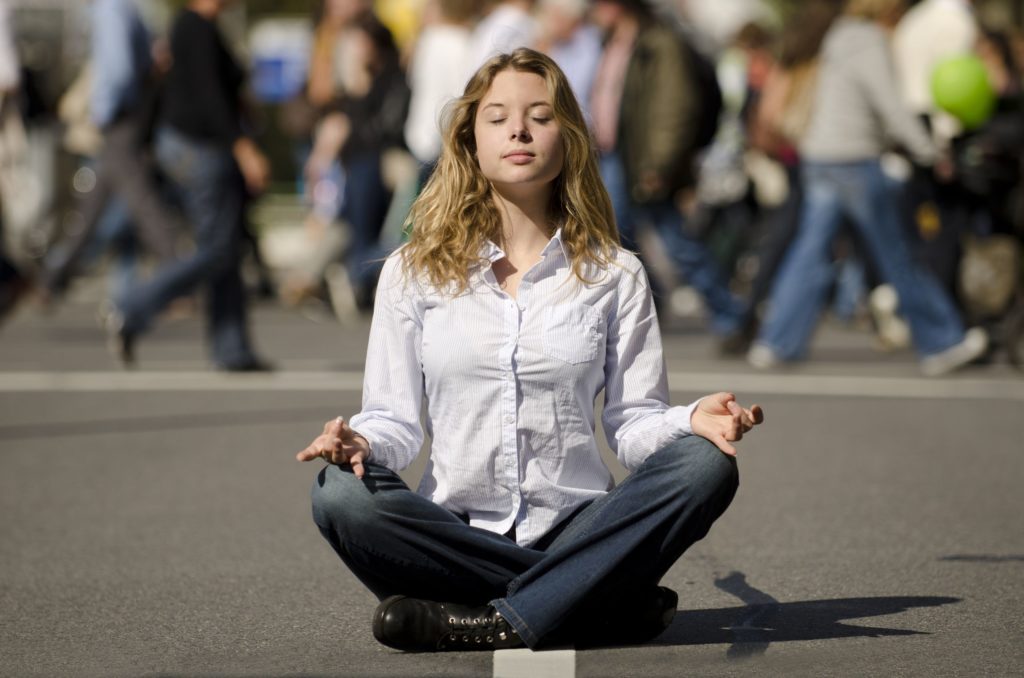 11471407 - woman meditating yoga in lotus position on busy urban street