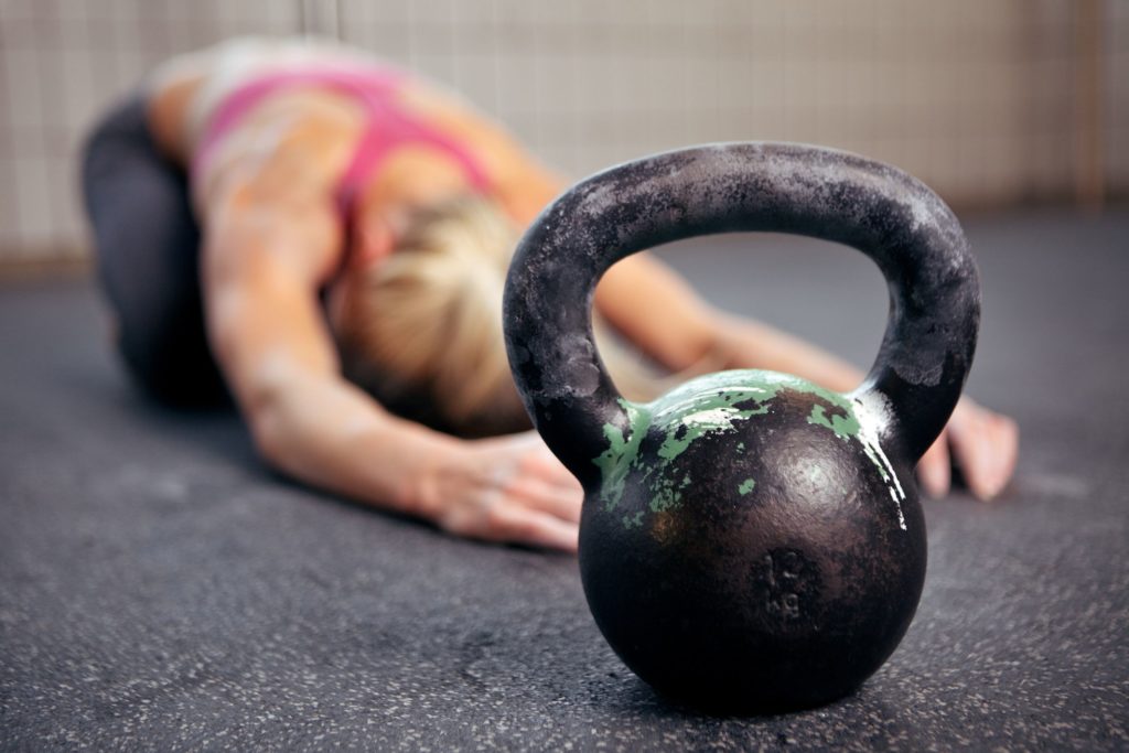 14158006 - young woman stretching her back after a heavy kettlebell workout in a gym