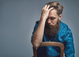 Depressed man with hand on forehead over gray