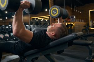 Caucasian male weightlifter bench-pressing in fitness center