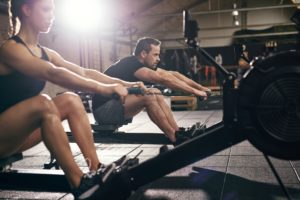 Sportsmen doing exercises with rowing machine together