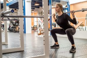 Young woman does barbell squats in modern gym